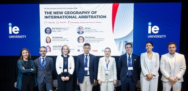 A group of professionals stands in front of a banner about international arbitration at IE University.