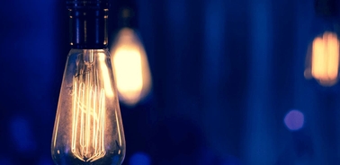 A close-up of a glowing filament light bulb against a blurred blue background.