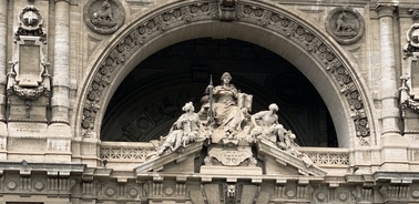 Statue of a seated figure flanked by two smaller figures on top of an ornate building facade.