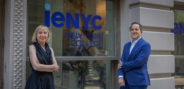 Two individuals stand in front of a college building with a prominent sign.