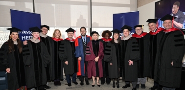 A group of graduates and faculty members in academic regalia pose for a photo at a graduation ceremony.