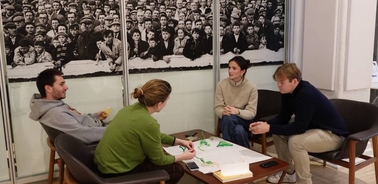 A group of four people is engaged in a discussion around a table in a modern workspace.