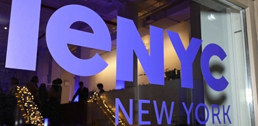 Window display with the text 'IENYC NEW YORK' illuminated in purple on glass, viewed from the street.