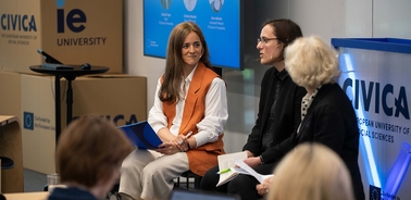A panel discussion featuring three women sitting on stage in a university setting.
