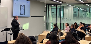A speaker presenting in a classroom setting with students attentively listening.
