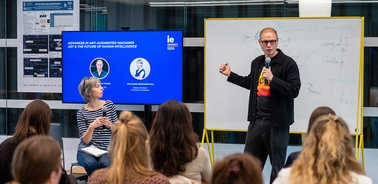A speaker is presenting on stage while an audience listens attentively.