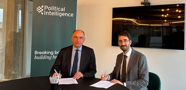 Two men signing a document at a table with a backdrop featuring the words 'Political Intelligence'.