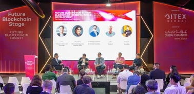 A panel discussion at a blockchain conference with speakers sitting on a stage in front of an audience.