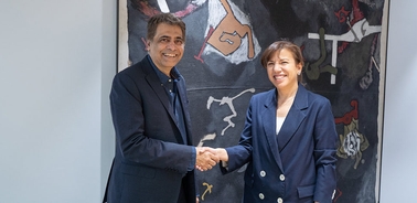 Two people are shaking hands in front of an abstract painting.