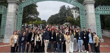 A large group of people posing for a photo in front of a decorative arch in a park.