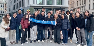 A diverse group of students gathered outdoors holding a banner for IE University.