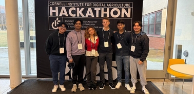 A group of six individuals posing for a photo in front of a hackathon backdrop.