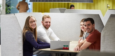 A group of four people smiling and sitting at a table in a modern office setting.