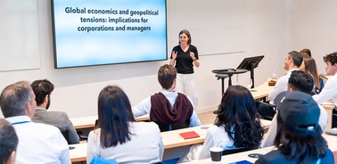A speaker presents on global economics and geopolitical tensions to an audience in a classroom setting.