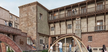 People exploring a rustic historical building with arched bridges and balcony.