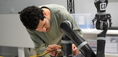 A person is working on connecting wires to a robotic arm in a lab setting.