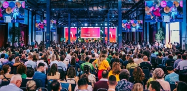 A packed audience attending a large event in a spacious venue with multiple screens displaying content.
