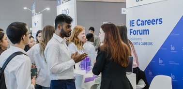 People engaging in conversation at a career forum event with IE Careers Forum banners visible.