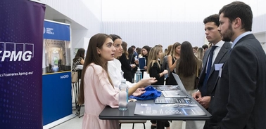 People engage in a conversation at a KPMG career booth in a professional event.