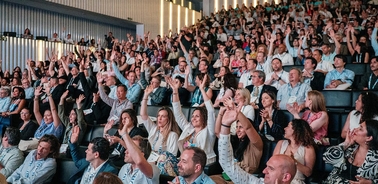 A large crowd enthusiastically raising their hands at an event.