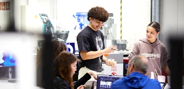 A young man and woman are engaging with attendees at a technology expo booth.