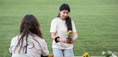 A young woman plants flowers in a pot on a grassy field.