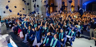 A large group of graduates celebrating by throwing their caps in the air during a graduation ceremony.