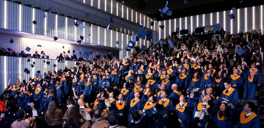 A large group of graduates in blue and yellow gowns celebrating in an auditorium