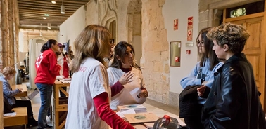 A group of people interacting at a venue, with some in red shirts providing information.