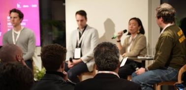 A panel discussion taking place with individuals seated on stage and an audience in view.