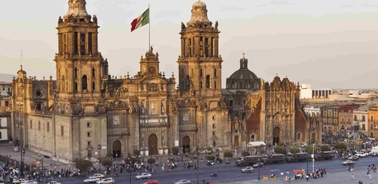 View of a large historic cathedral facing a spacious square with people and cars, and a large flag waving in the center.