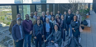 A diverse group of people standing together on a rooftop with a cityscape in the background.