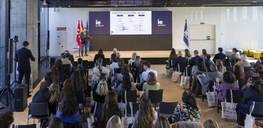 A speaker presenting at a conference in a modern venue with an audience of attentive listeners.