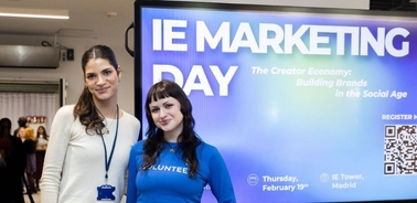 Two women standing in front of a promotional banner for IE Marketing Day.