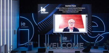 A virtual lecture setup featuring Joachim Frank on a large screen at a university event.