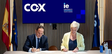 Two individuals are signing a document at a formal event with university branding in the background.