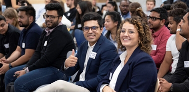 A group of young adults in a conference setting, with one man giving a thumbs up.