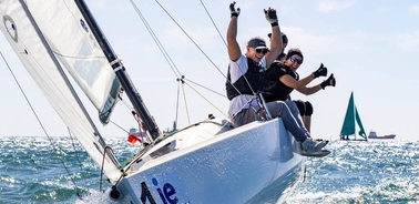 Three people are enjoying sailing on a sunny day, showing excitement and thumbs up.