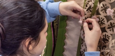 A person is delicately working on a decorative fabric with small embellishments.
