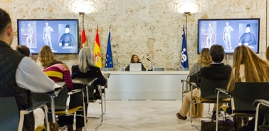 A person giving a presentation in front of an audience with images displayed on screens behind them.