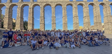 A large group of people gathered in front of a historic aqueduct.