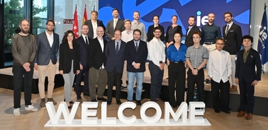 A group of diverse people posing together in an indoor setting with a 'WELCOME' sign in the foreground.