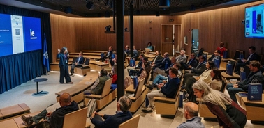 A presentation taking place in a modern auditorium with an audience seated and a speaker in front of a large screen.