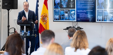 A speaker presenting in front of an audience with visual aids on a screen.