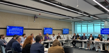 A large group of professionals engaged in a business meeting around a U-shaped table in a modern conference room.