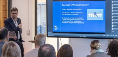 A man presents a medical concept on patient selection at a conference to an attentive audience.