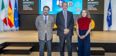 Three people, two men and one woman, standing in front of a presentation about global economy studies at a university.