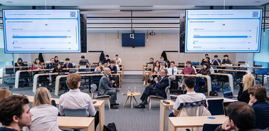 A classroom setting with students engaged in a discussion while viewing presentation screens.