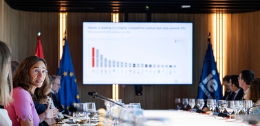 A meeting in a modern conference room with a presentation on a screen and attendees around a table.