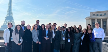 A diverse group of young professionals posing together with the Eiffel Tower in the background.